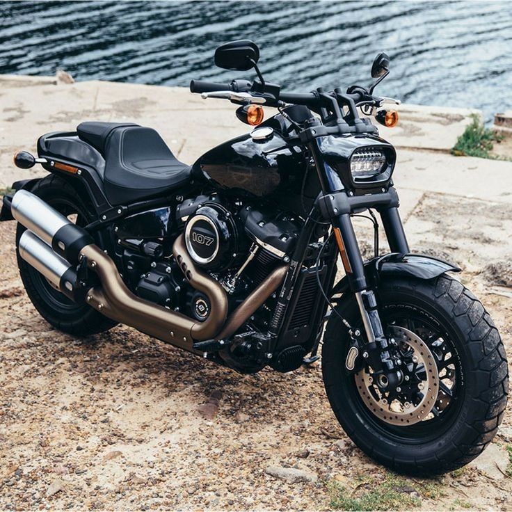 a black motorcycle parked on top of a dirt field next to the water and grass