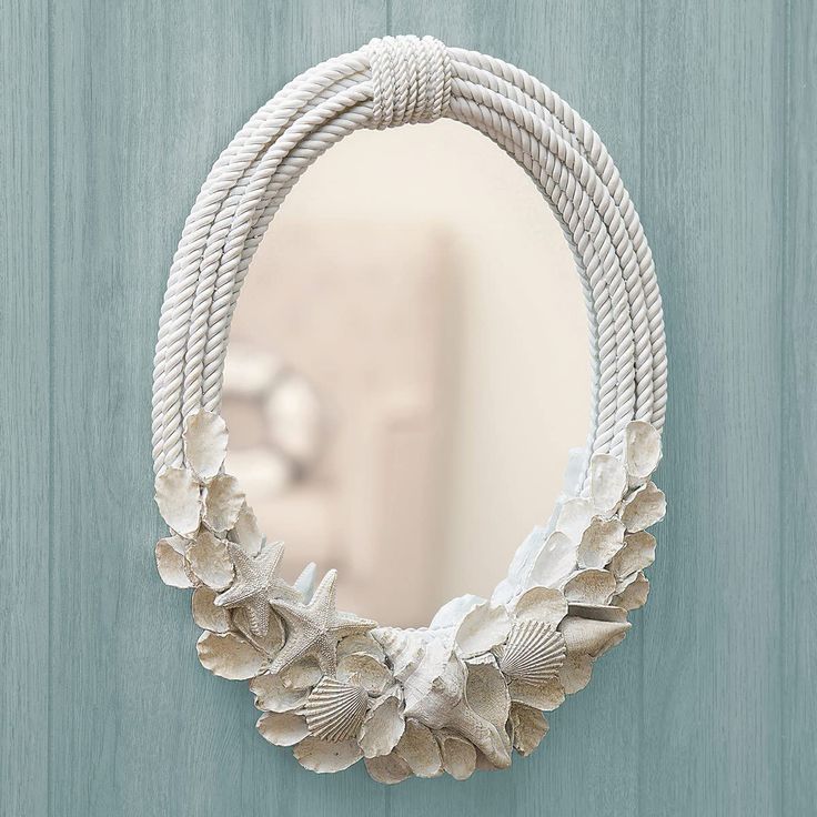 a white rope mirror hanging on the side of a blue door with flowers in it