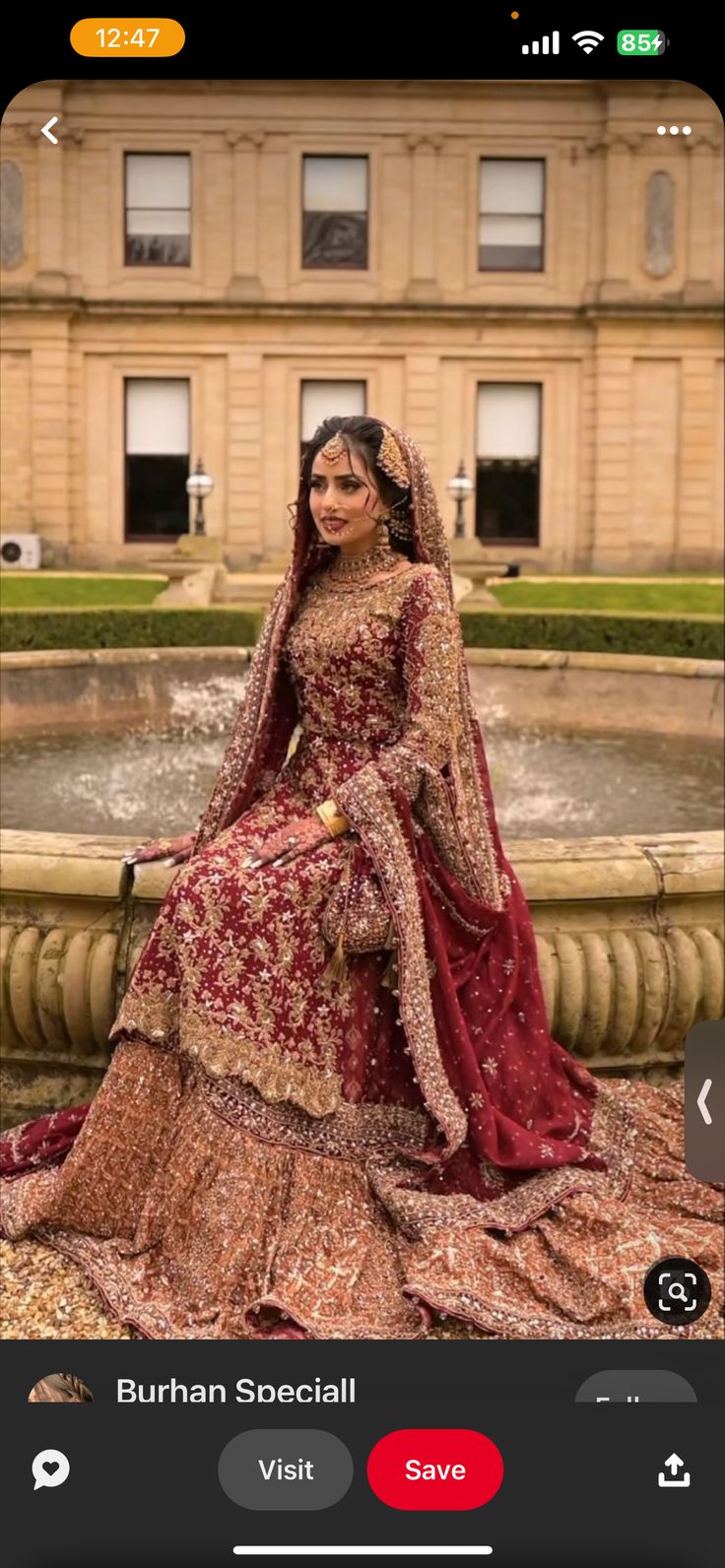 a woman in a red and gold bridal gown sitting on a fountain with an ornate building in the background