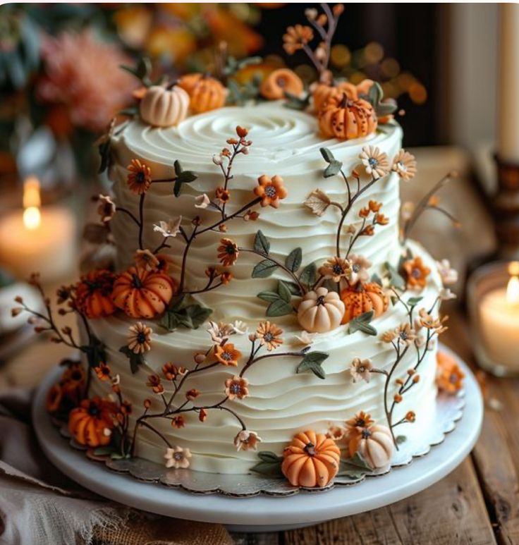 a three layer cake decorated with pumpkins and flowers on a table next to candles