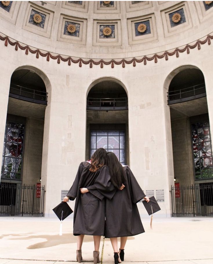 two women standing in front of a building with their back to the camera, both wearing black robes