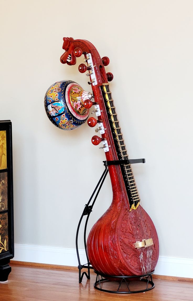 a red instrument sitting on top of a hard wood floor next to a white wall