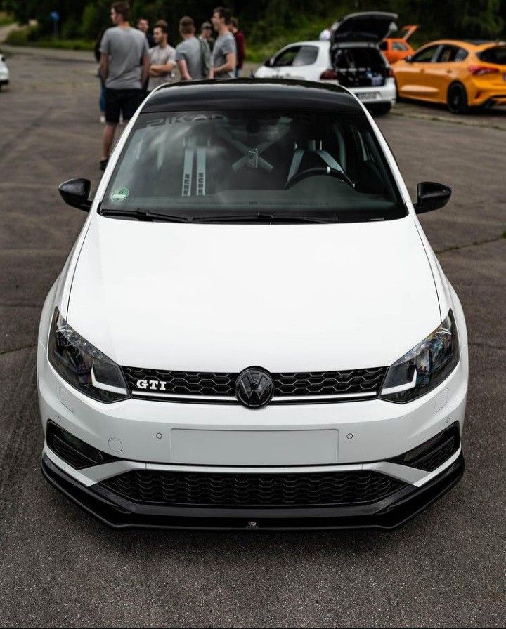 the front end of a white car parked in a parking lot with other cars behind it