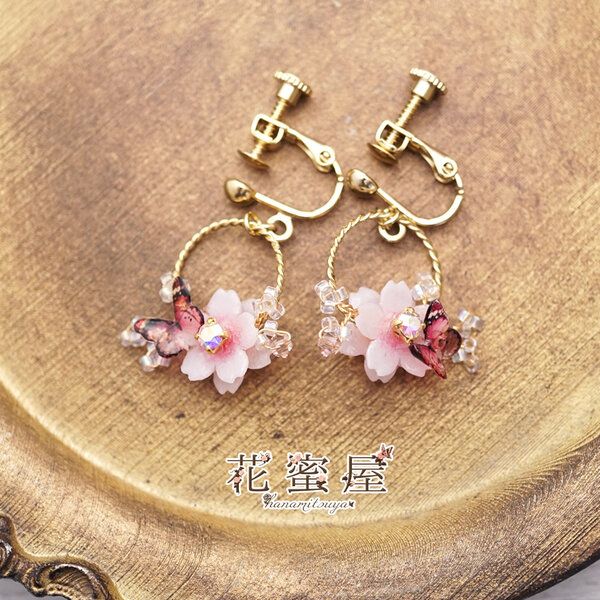 two pink flowers are hanging from gold earwires on a wooden surface with chinese writing