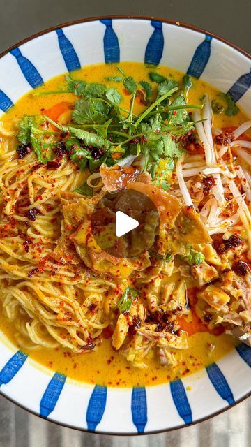 a bowl filled with noodles and vegetables on top of a blue and white striped plate