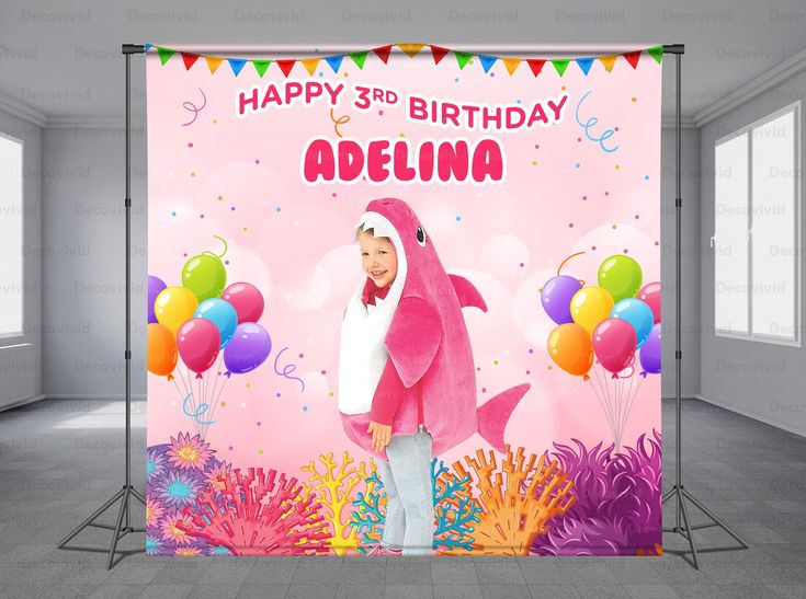 a birthday banner with a pink shark and balloons on the wall in an empty room