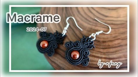 the earrings are made with black thread and red beads on them, sitting on top of a wooden piece