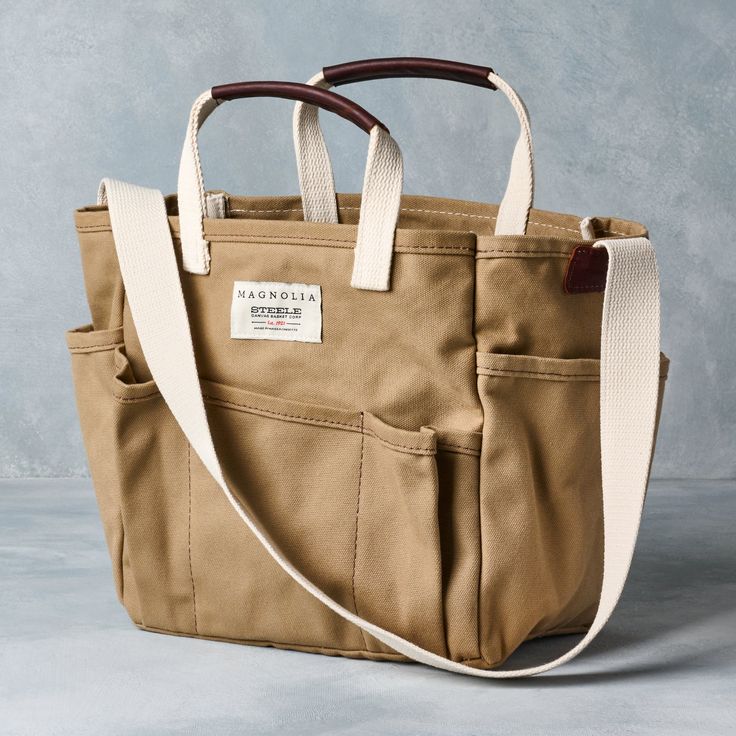 Made in the USA and designed with gardeners, craftsmen, and shoppers in mind, the Magnolia Steel Canvas Utility Tote boasts nine pockets to hold everything you need. Crafted from heavy duty duck canvas in a beautiful green hue and featuring leather grip handles and a reinforced shoulder strap, this exclusive bag also includes a Magnolia logo.For more options, shop our Garden and Gardening Tools collections Magnolia Logo, Steele Canvas, Hand Bags Ideas, Garden Tool Bag, Leaf Bag, Jeans Crafts, Utility Tote Bag, Book Tote Bag, Utility Tote