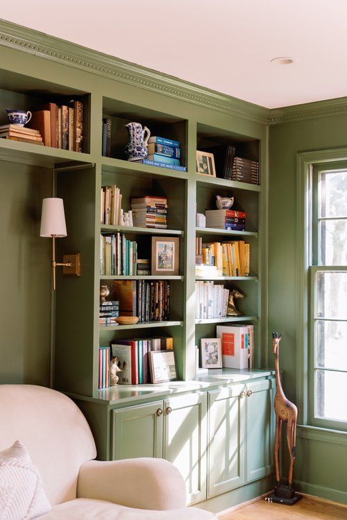 a living room filled with lots of green bookshelves next to a white couch