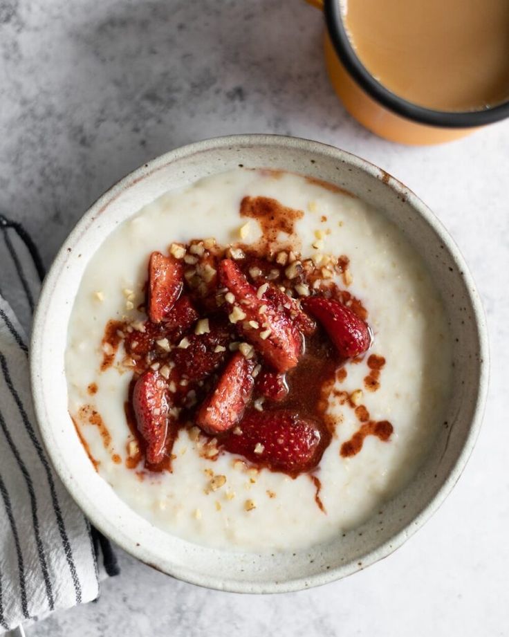 a bowl of oatmeal with strawberries and nuts next to a cup of coffee