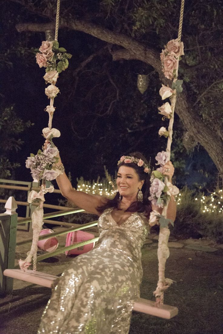 a woman is sitting on a swing with flowers in her hair and wearing a sequin dress