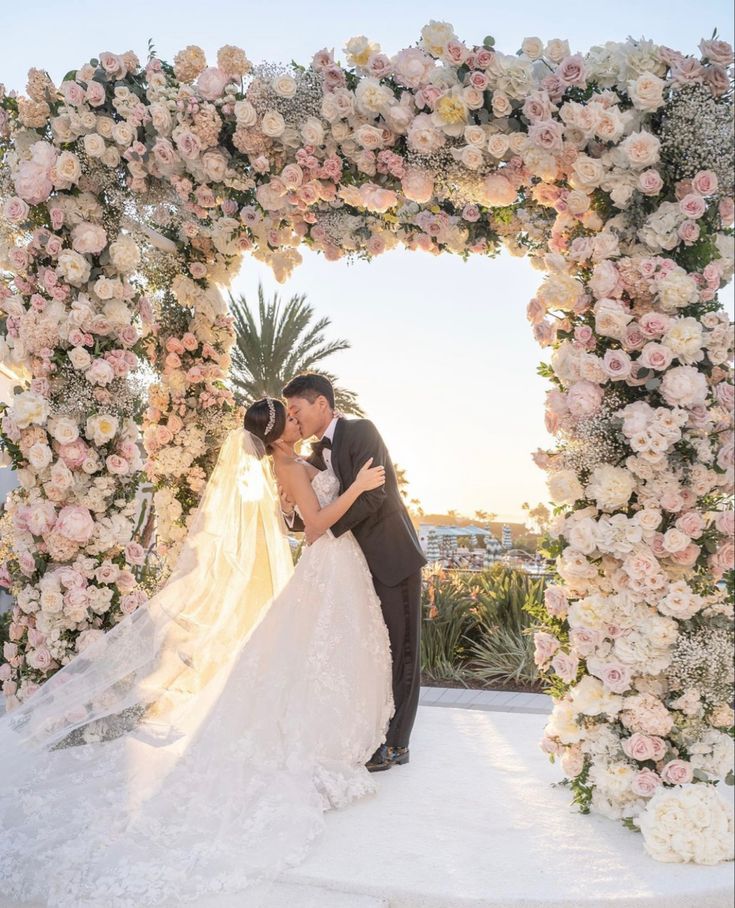 a bride and groom kissing in front of a floral arch at the end of their wedding day