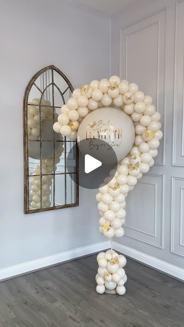 a balloon arch with white balloons hanging from it's sides in front of a mirror