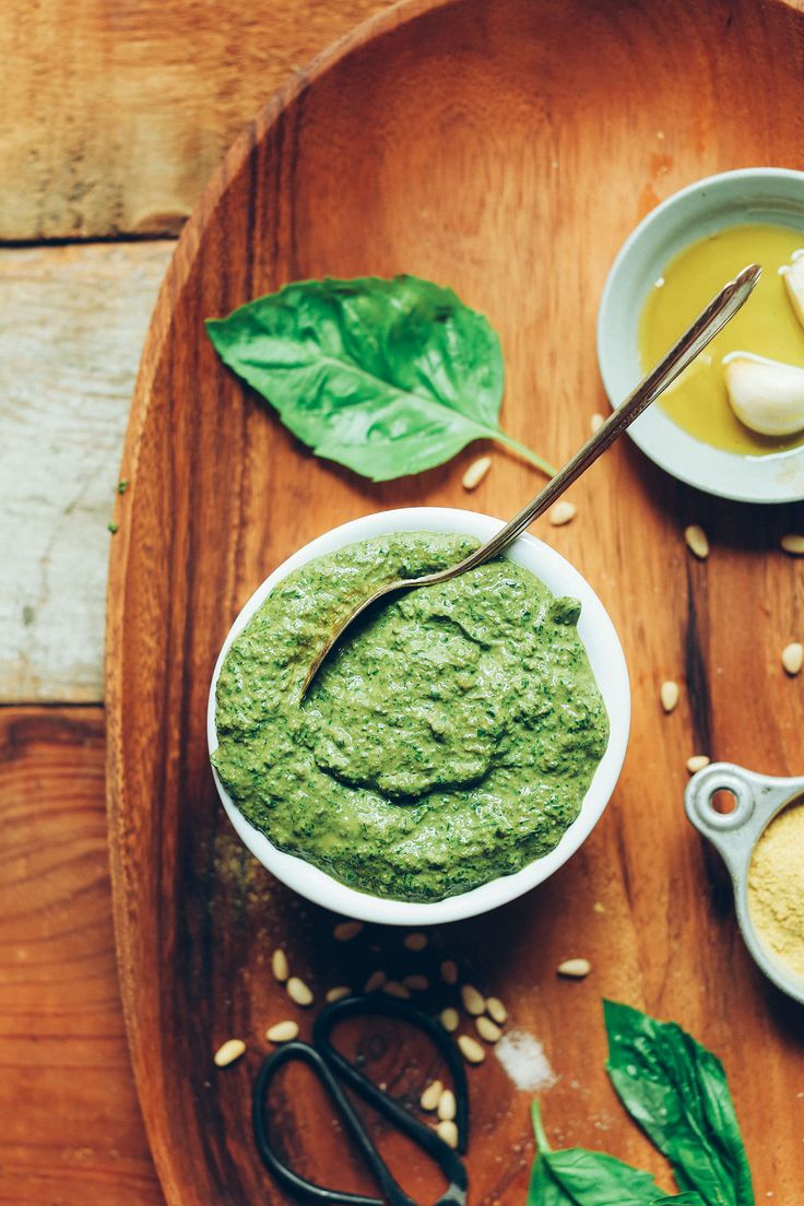 a wooden tray topped with two bowls filled with green dips and garlic on top of it