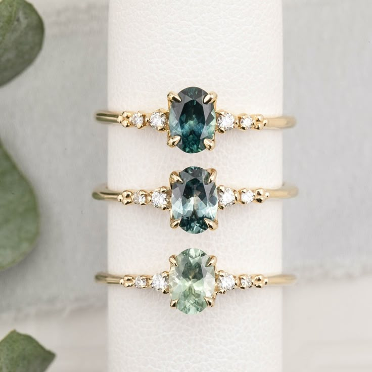 three rings with different colored stones on top of each other next to a succulent plant