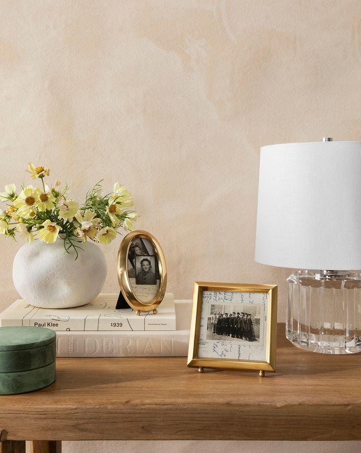 a table topped with books and a vase filled with flowers next to a lamp on top of a wooden table