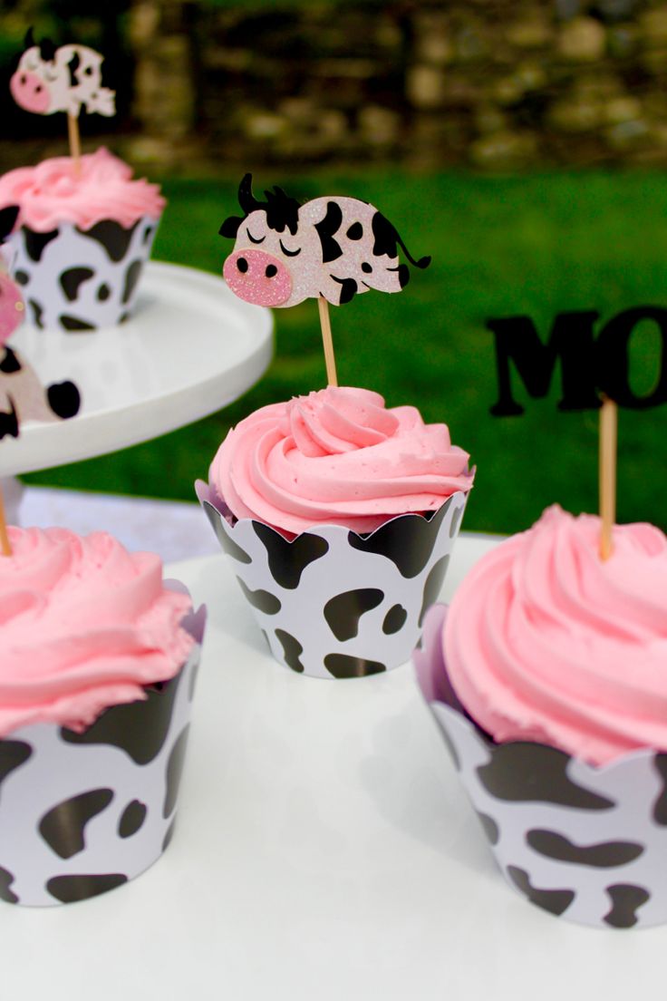 cupcakes decorated with pink frosting and black cow designs on top of white plates