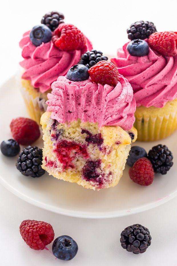 two cupcakes with pink frosting and raspberries on a white plate