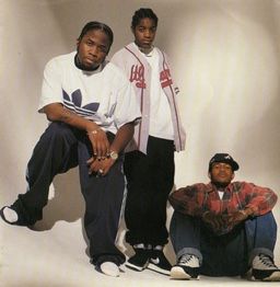 three young men sitting next to each other in front of a white background with one man holding a skateboard