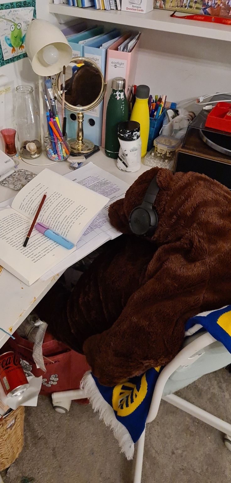 a messy desk with books, headphones and other items on it in a cluttered room