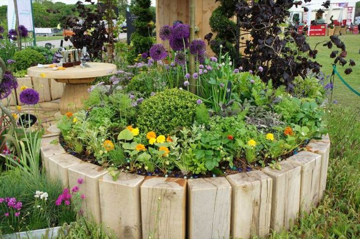 a garden filled with lots of different types of flowers and plants next to a wooden structure