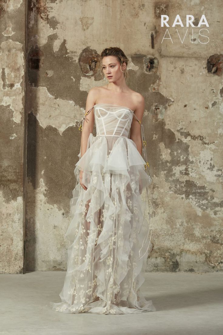 a woman in a white dress standing on a concrete floor with an old wall behind her