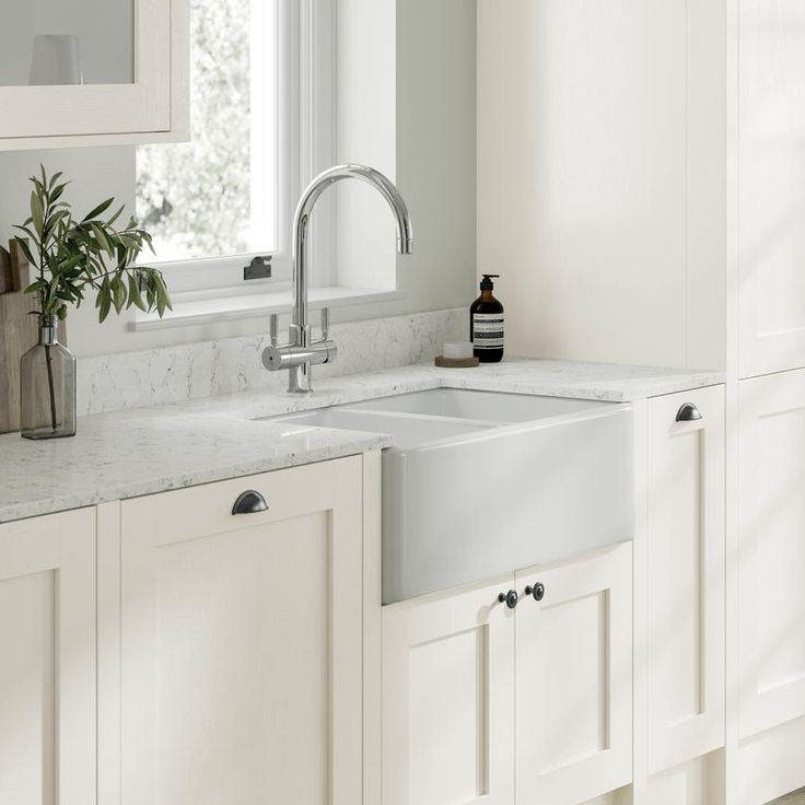 a kitchen with white cabinets and marble counter tops is pictured in this image, there are two plants on the window sill