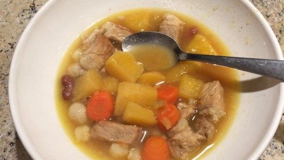 a white bowl filled with soup and meat on top of a granite counter next to a spoon