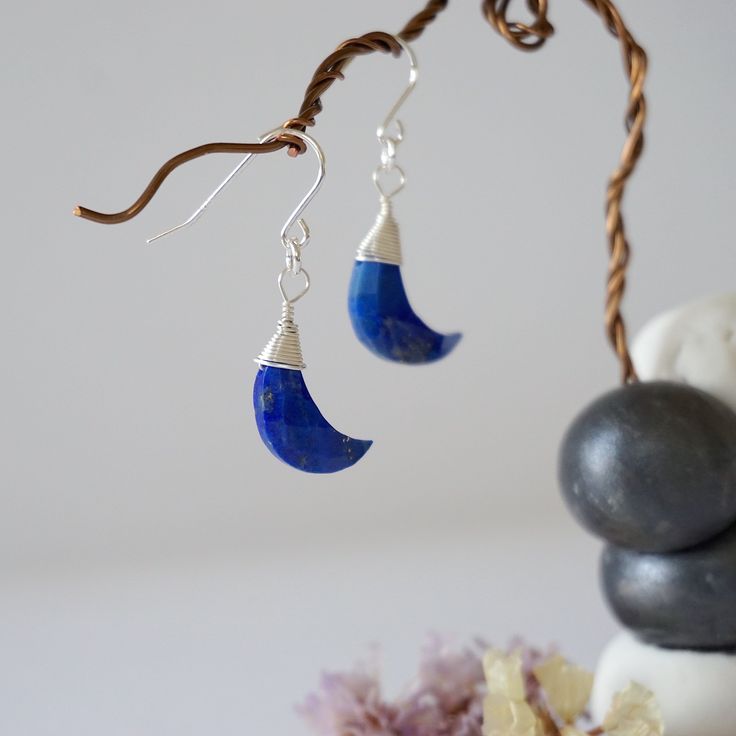 Discover inner truth with the energies of these uniquely crafted lapis lazuli earrings. Our lapis lazuli moon earrings are known for: HANDMADE ORIGINAL DESIGN - We customize each lapis lazuli earring to the unique shape of its stone. This process makes your moon earrings truly one of a kind. AUTHENTIC CRYSTALS & ALLERGY FREE MATERIALS - Your lapis lazulis are authentic and natural. Our artists sort through hundreds of lapis lazulis to find yours. We only use nickel-free, lead-free and allergy-fr Blue Crescent Moon Charm Earrings, Blue Moon Shaped Sterling Silver Earrings, Blue Moon-shaped Sterling Silver Earrings, Blue Crescent Earrings As A Gift, Bohemian Blue Moon Shaped Earrings, Bohemian Blue Moon-shaped Earrings, Wire Wrapped Lapis Lazuli Dangle Earrings, Lapis Lazuli Natural Stones Drop Earrings, Blue Lapis Lazuli Earrings