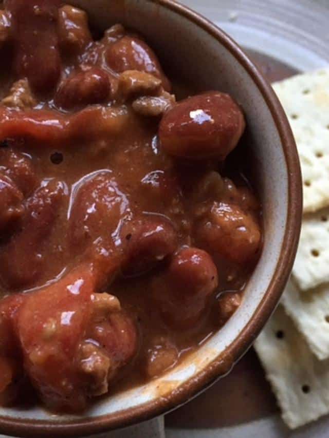 a bowl filled with meat and veggies next to crackers