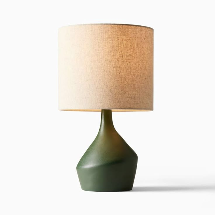 a green table lamp with a white shade on it's base and a beige linen lampshade