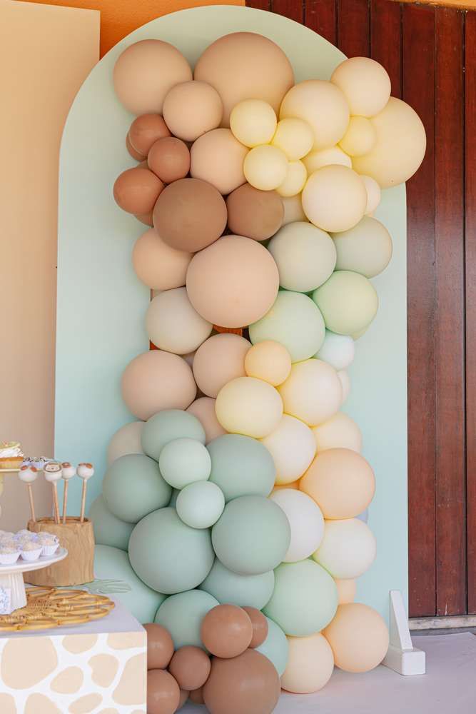 an arch made out of balloons is shown in front of a table with desserts on it