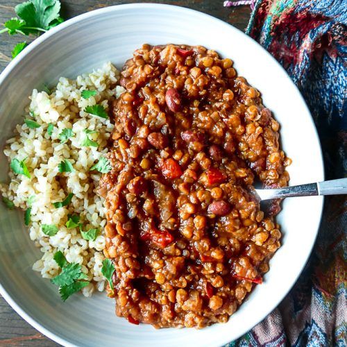 a white bowl filled with beans and rice on top of a wooden table next to a napkin