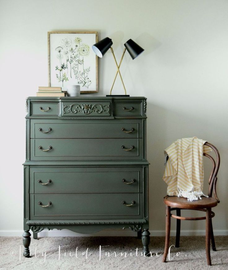 a green dresser with two lamps on top and a chair in the corner next to it