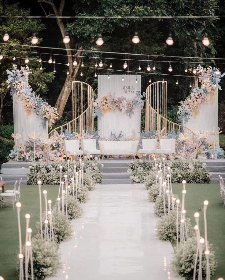 an outdoor wedding ceremony setup with candles and floral arrangements on the aisle, surrounded by greenery