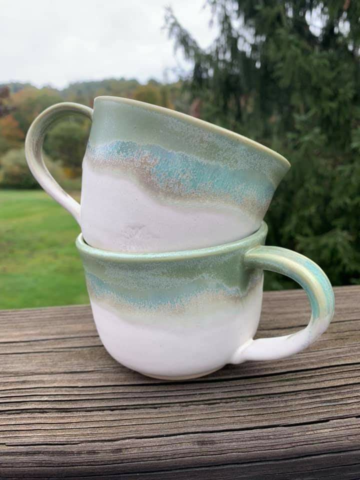 two coffee cups sitting on top of a wooden table next to some grass and trees