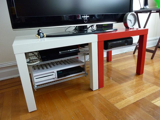 a flat screen tv sitting on top of a white table next to a red shelf