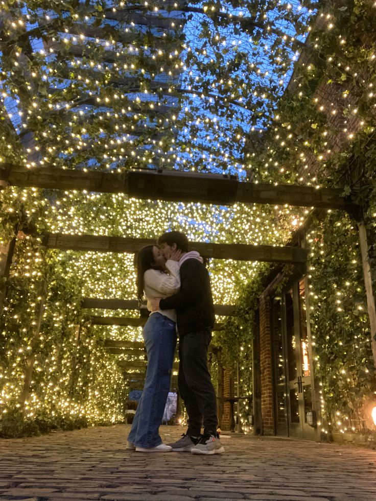 two people kissing under a canopy covered in lights