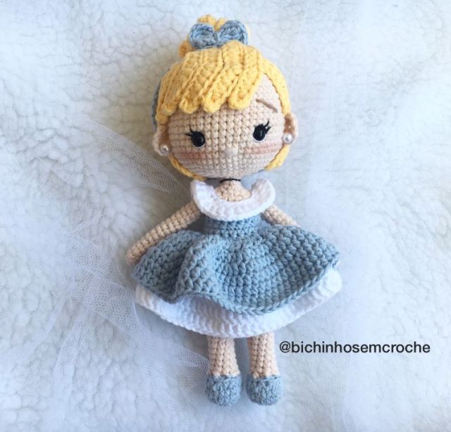 a crocheted doll is laying on a white blanket with a blue dress and headband