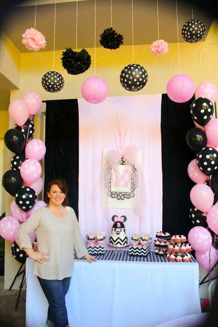 a woman standing in front of a table with black and pink balloons on it,