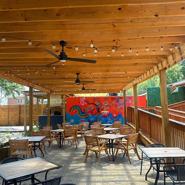 an outdoor dining area with tables and chairs under a wooden roof over looking a colorful mural