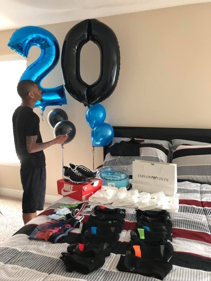 a man standing in front of a bed with blue balloons and an oversized number balloon