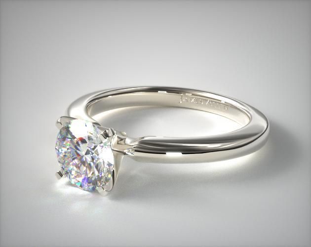 a white gold engagement ring with a round brilliant cut diamond in the center, on a plain surface