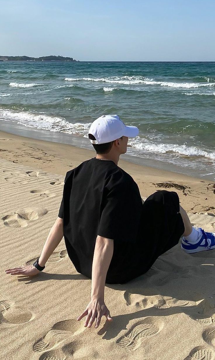 a man sitting on the beach with his feet in the sand looking out at the ocean