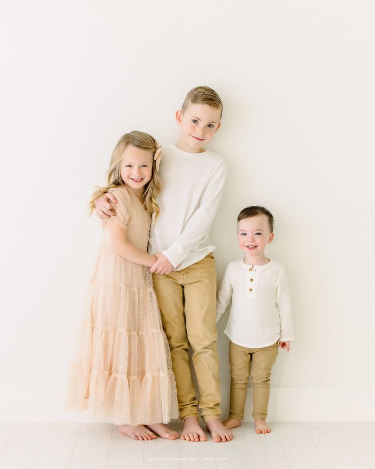 three children standing next to each other in front of a white wall