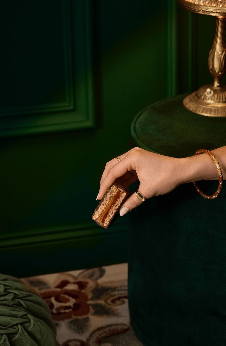 a woman's hand holding a piece of bread in front of a green chair