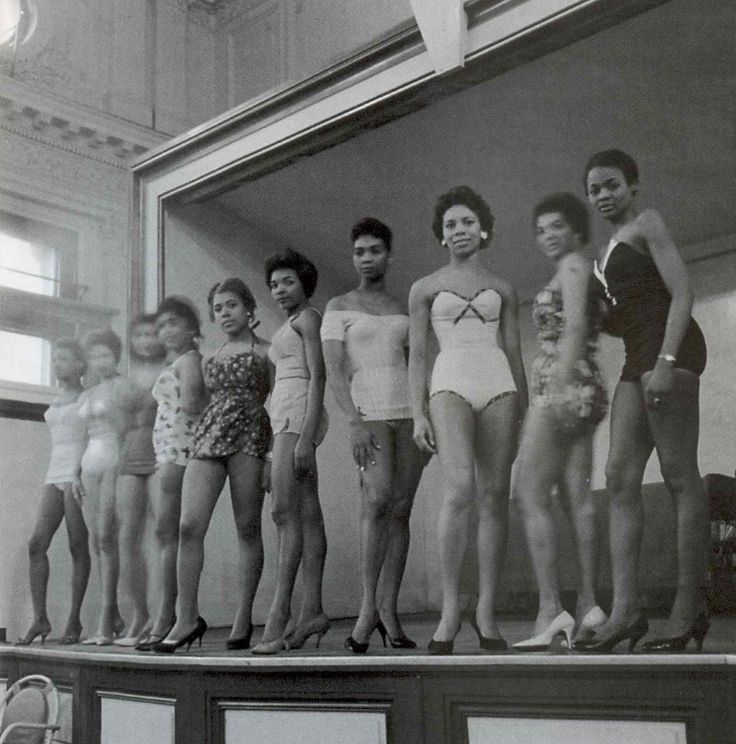 an old black and white photo of people in bathing suits standing on a platform with their hands behind their backs