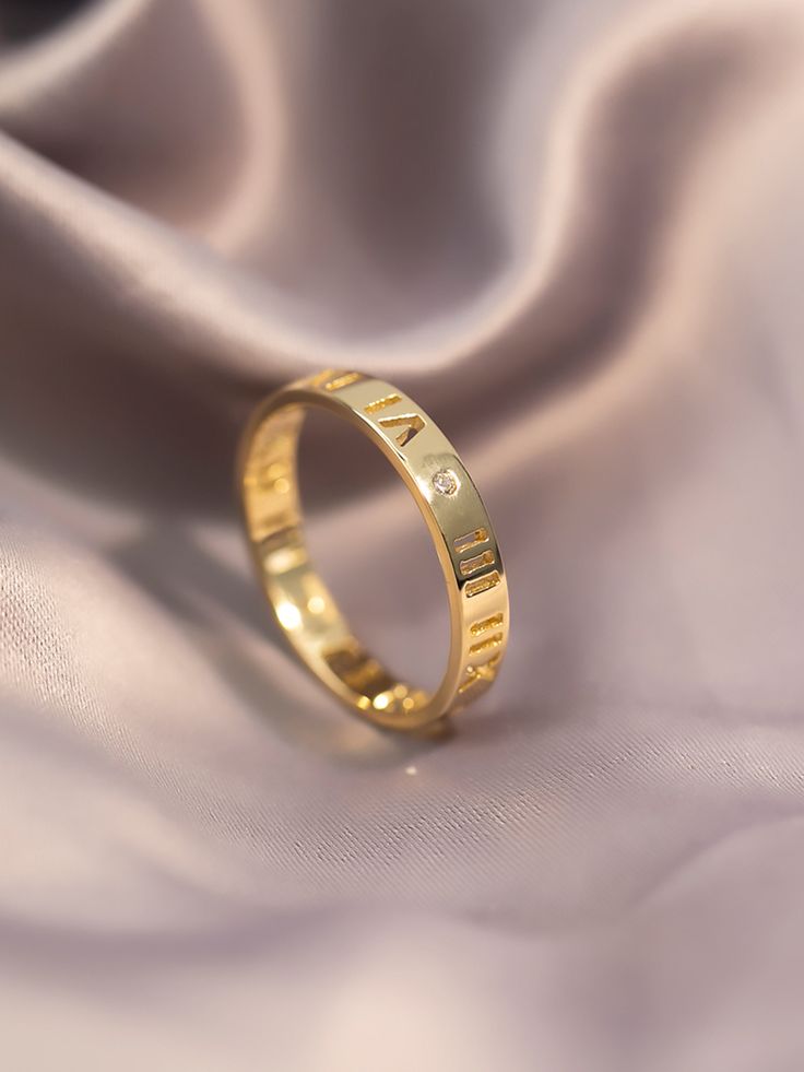 a gold wedding band with the word love written on it, laying on a satin fabric