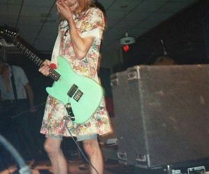 a man holding a green guitar while standing in front of a microphone and other people