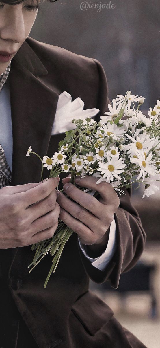 a man wearing a suit and tie holding a bouquet of daisies in his hands